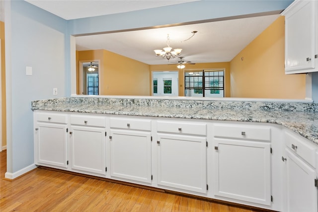 kitchen with ceiling fan with notable chandelier, light wood-type flooring, kitchen peninsula, and white cabinetry