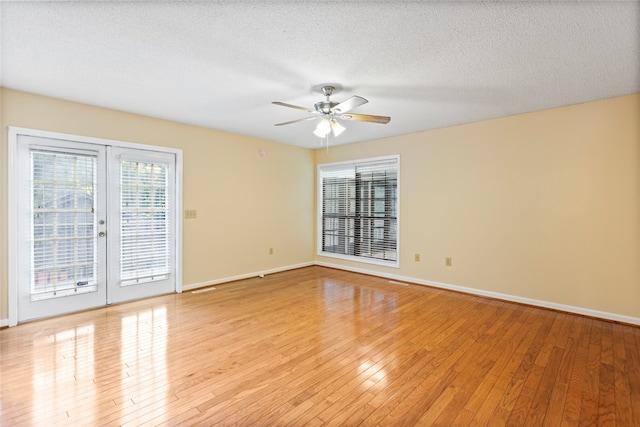 empty room with a textured ceiling, light hardwood / wood-style flooring, french doors, and a wealth of natural light