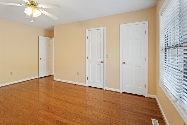 unfurnished bedroom featuring hardwood / wood-style floors, ceiling fan, and multiple closets