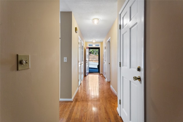 hallway with a textured ceiling and light hardwood / wood-style flooring