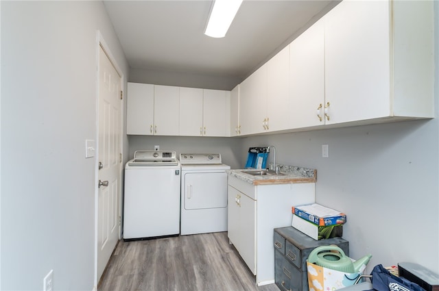 washroom with washing machine and clothes dryer, sink, light hardwood / wood-style flooring, and cabinets