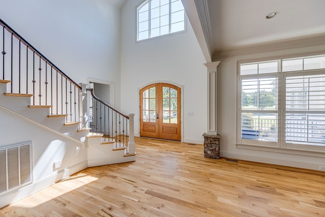 foyer entrance with french doors, light hardwood / wood-style flooring, a towering ceiling, and ornamental molding