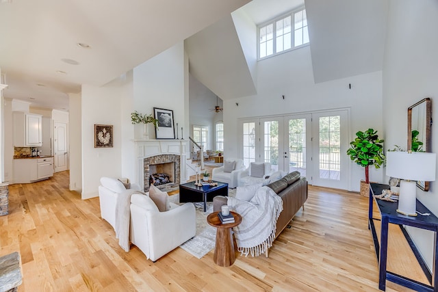 living room with a fireplace, light wood-type flooring, a high ceiling, ceiling fan, and french doors