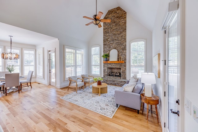 living room featuring ceiling fan with notable chandelier, light hardwood / wood-style flooring, a fireplace, and high vaulted ceiling