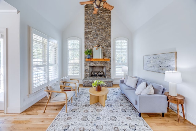 living room featuring high vaulted ceiling, a stone fireplace, hardwood / wood-style floors, crown molding, and ceiling fan