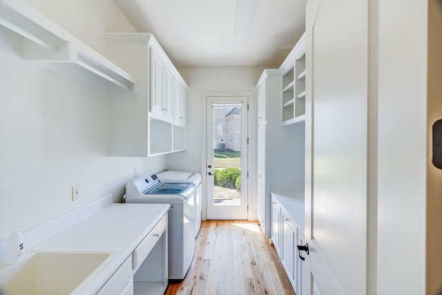 washroom featuring washing machine and dryer, sink, light hardwood / wood-style flooring, and cabinets