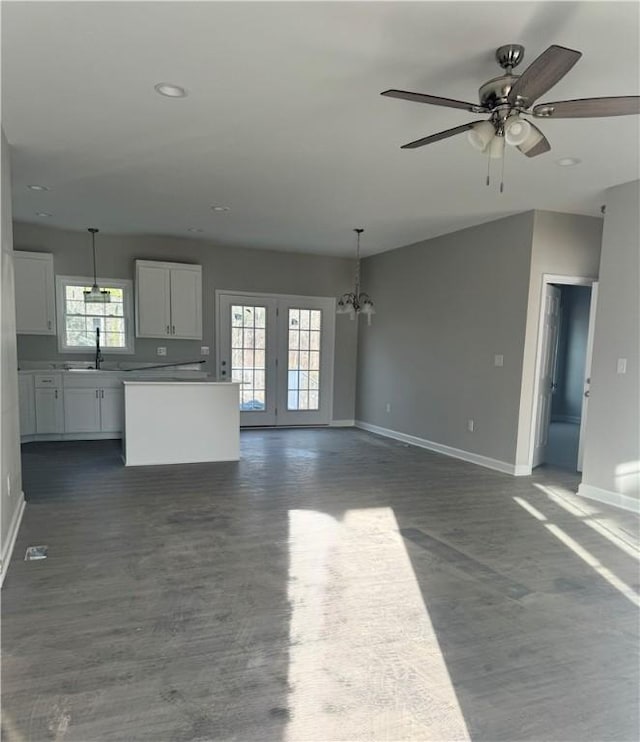 unfurnished living room featuring baseboards, dark wood-style floors, ceiling fan with notable chandelier, a sink, and recessed lighting