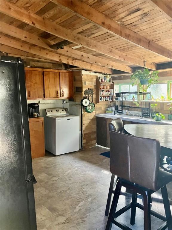 kitchen featuring concrete flooring, wooden ceiling, freestanding refrigerator, brown cabinets, and washer / dryer