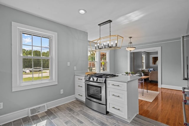 kitchen with light hardwood / wood-style flooring, hanging light fixtures, stainless steel gas range, a chandelier, and white cabinets