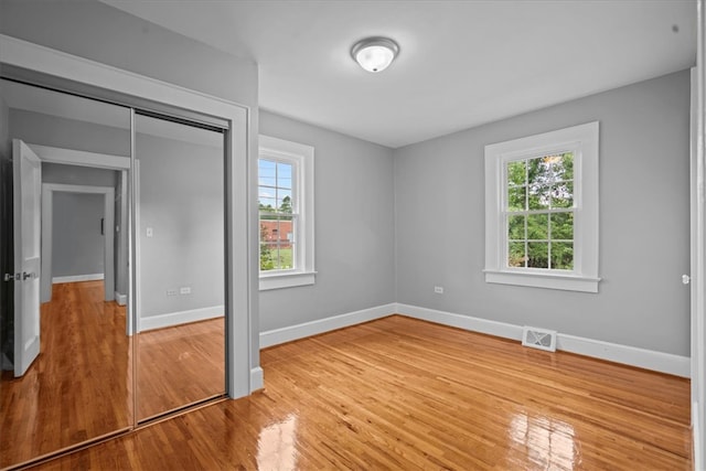 unfurnished bedroom with light hardwood / wood-style floors, multiple windows, and a closet