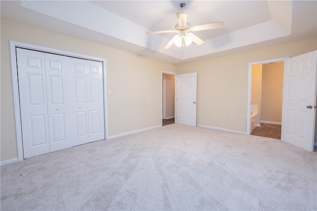 unfurnished bedroom with light carpet, a closet, a raised ceiling, and ceiling fan