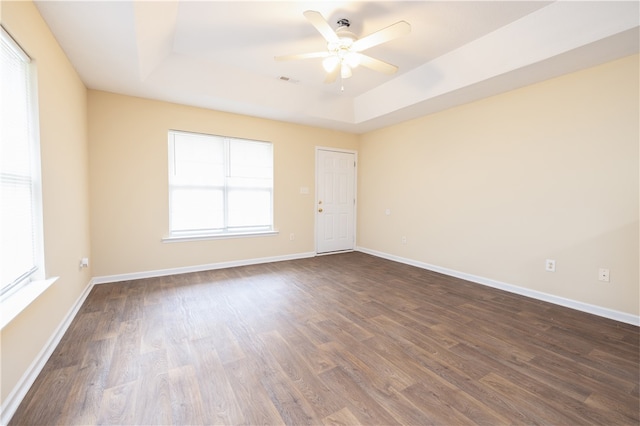 empty room featuring a tray ceiling, dark wood-type flooring, and ceiling fan