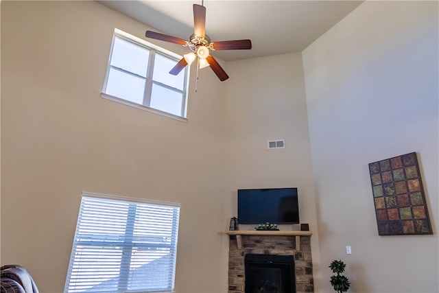 living room with ceiling fan, a fireplace, and a towering ceiling