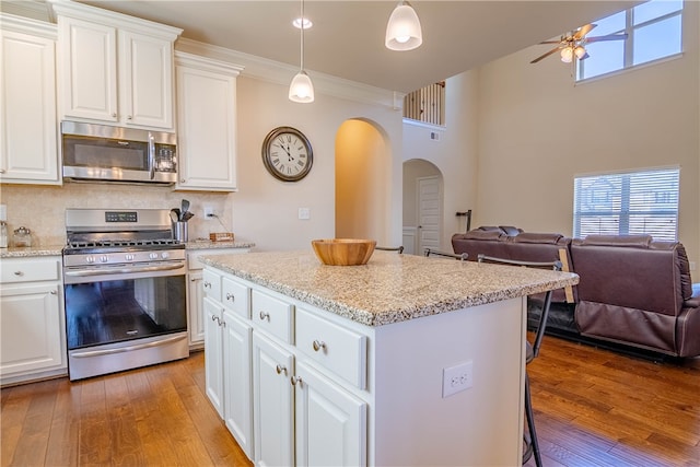 kitchen featuring white cabinets, hanging light fixtures, stainless steel appliances, a kitchen breakfast bar, and light wood-type flooring