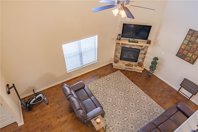 living room featuring ceiling fan, dark hardwood / wood-style floors, and a stone fireplace