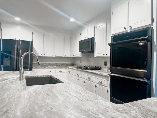 kitchen with sink, backsplash, white cabinetry, black appliances, and light stone countertops