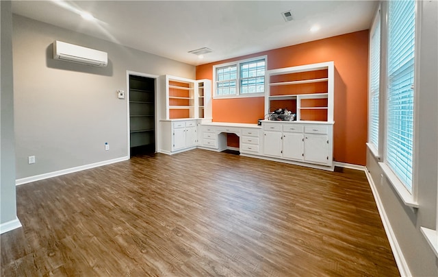 unfurnished living room featuring built in desk, dark hardwood / wood-style floors, and a wall mounted AC