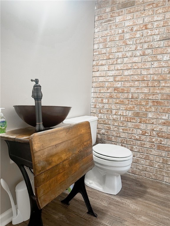 bathroom with wood-type flooring, toilet, sink, and brick wall