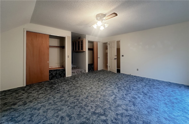 unfurnished bedroom featuring ceiling fan, dark carpet, a textured ceiling, a closet, and vaulted ceiling