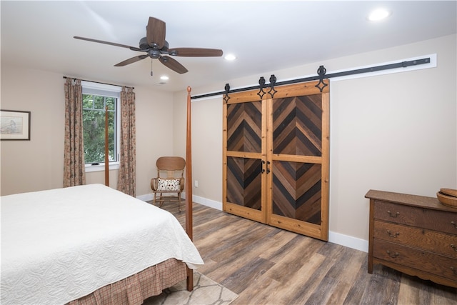 bedroom with a barn door, dark wood-type flooring, and ceiling fan