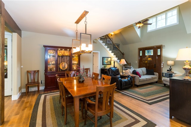 dining space with ceiling fan with notable chandelier, high vaulted ceiling, and light hardwood / wood-style flooring