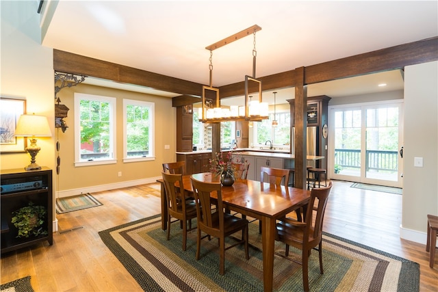 dining room featuring light wood-type flooring, beamed ceiling, plenty of natural light, and sink