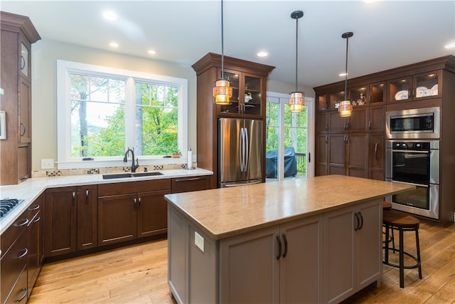 kitchen featuring light wood-type flooring, a center island, stainless steel appliances, sink, and decorative light fixtures