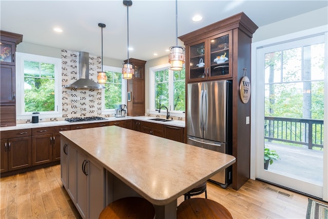 kitchen with sink, a kitchen island, wall chimney exhaust hood, light hardwood / wood-style flooring, and stainless steel appliances