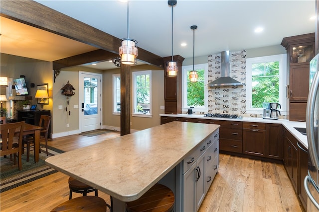 kitchen with wall chimney exhaust hood, plenty of natural light, light hardwood / wood-style floors, and a center island