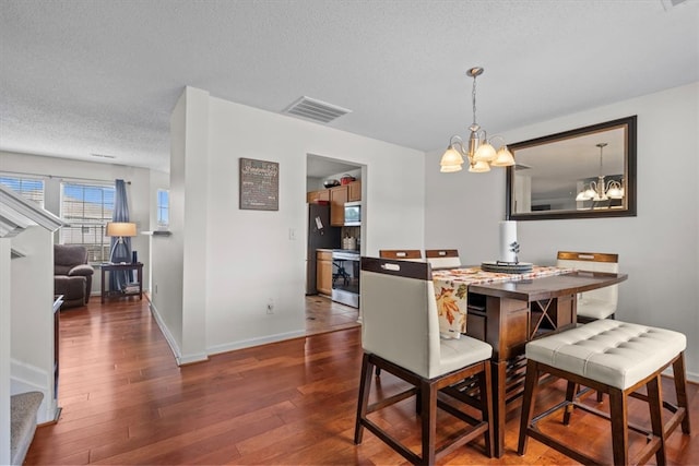 dining area featuring an inviting chandelier, a textured ceiling, and dark wood-type flooring