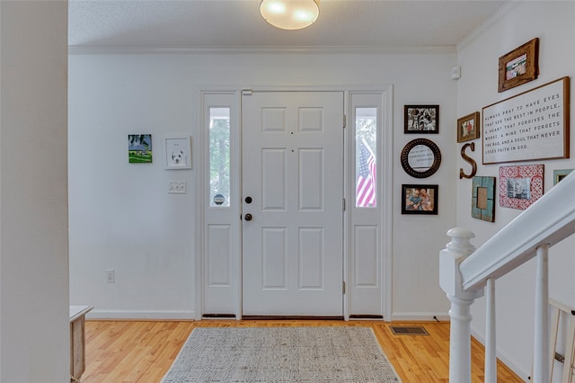 foyer entrance featuring a textured ceiling, light wood-type flooring, and crown molding