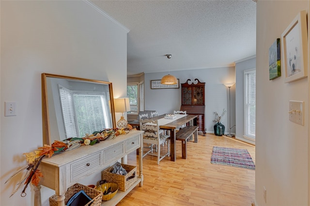 dining room featuring a textured ceiling, ornamental molding, and light hardwood / wood-style flooring