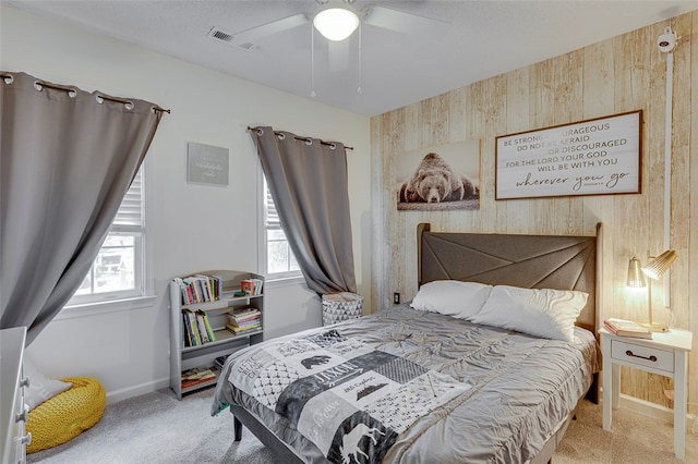 carpeted bedroom with ceiling fan, wood walls, and multiple windows