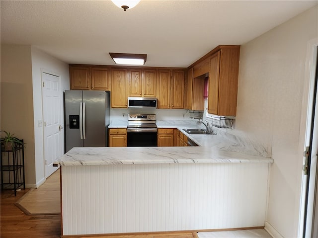 kitchen featuring appliances with stainless steel finishes, kitchen peninsula, a textured ceiling, light hardwood / wood-style flooring, and sink