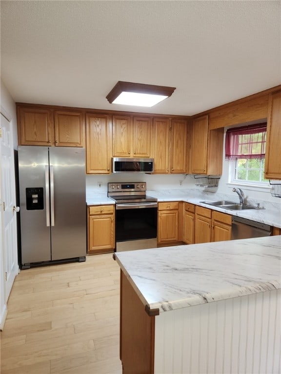 kitchen with appliances with stainless steel finishes, light wood-type flooring, sink, and kitchen peninsula