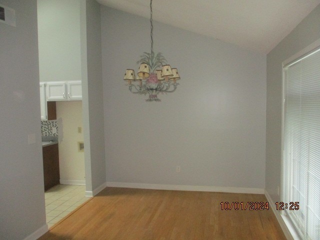 unfurnished dining area with lofted ceiling, an inviting chandelier, and light hardwood / wood-style flooring