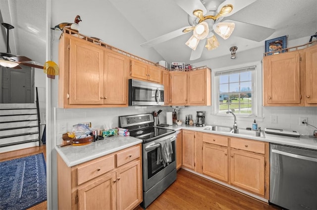 kitchen with sink, wood-type flooring, appliances with stainless steel finishes, light brown cabinetry, and vaulted ceiling