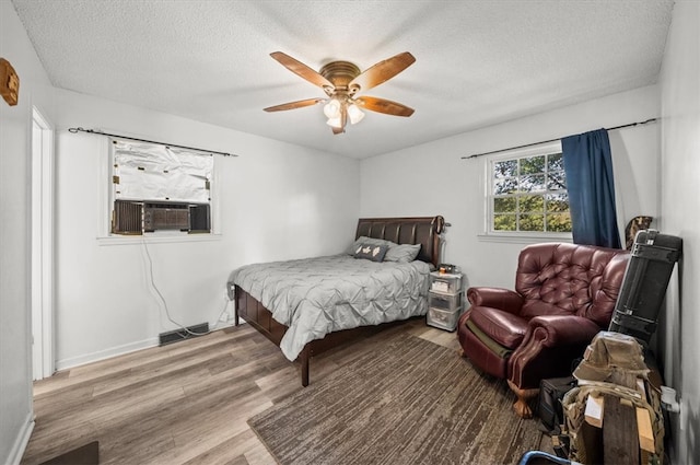 bedroom featuring cooling unit, hardwood / wood-style flooring, a textured ceiling, and ceiling fan