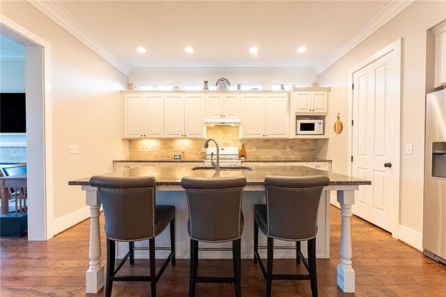 kitchen with crown molding, hardwood / wood-style flooring, an island with sink, decorative backsplash, and dark stone counters