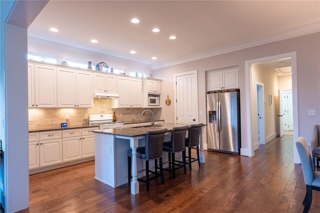 kitchen with sink, white cabinetry, a center island with sink, dark stone countertops, and white appliances