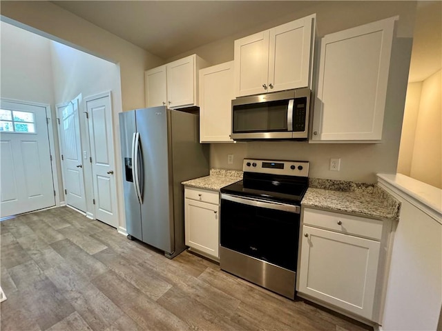 kitchen featuring white cabinets, light hardwood / wood-style floors, light stone counters, and appliances with stainless steel finishes