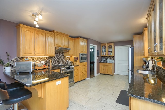 kitchen featuring sink, stainless steel appliances, backsplash, kitchen peninsula, and dark stone countertops