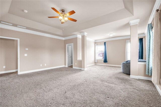 carpeted spare room featuring a tray ceiling, crown molding, decorative columns, a ceiling fan, and baseboards