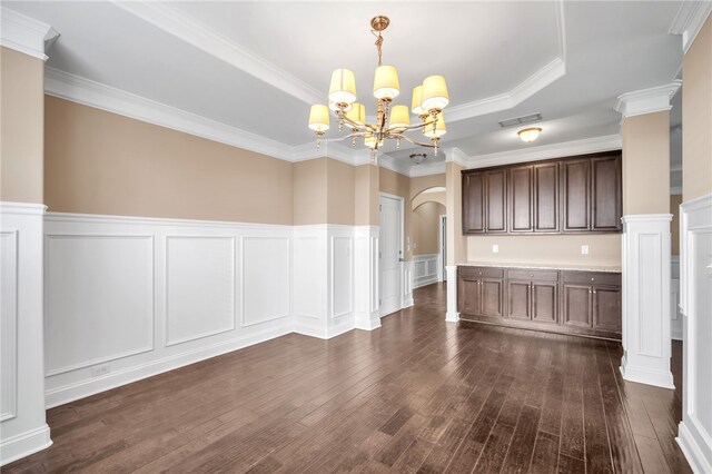 unfurnished dining area featuring visible vents, arched walkways, a raised ceiling, dark wood-style flooring, and ornate columns