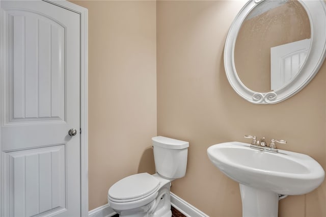 half bathroom with a sink, toilet, and baseboards