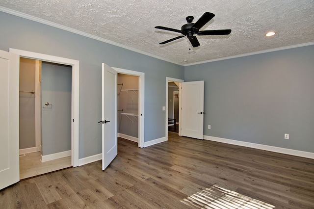 unfurnished bedroom featuring a spacious closet, ceiling fan, hardwood / wood-style floors, and a textured ceiling