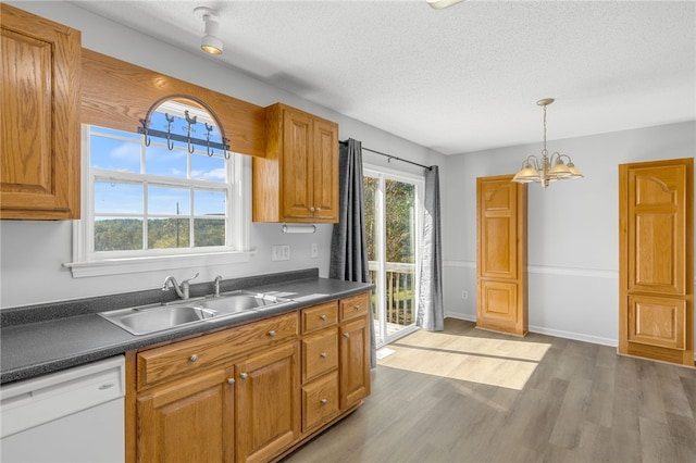 kitchen with white dishwasher, sink, wood-type flooring, pendant lighting, and an inviting chandelier