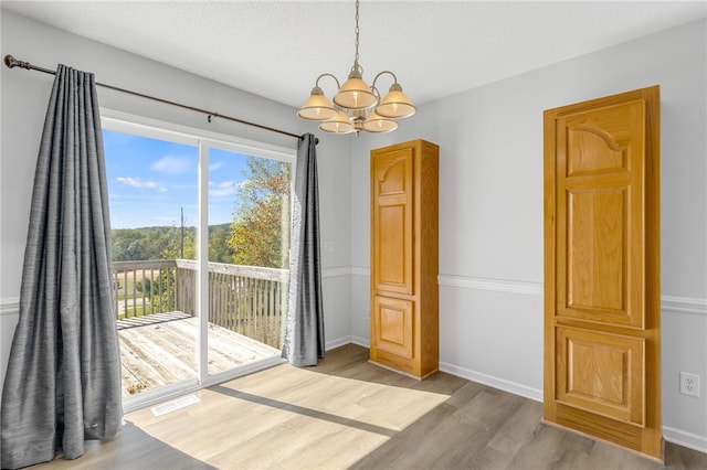 unfurnished dining area with hardwood / wood-style floors, a textured ceiling, and a notable chandelier