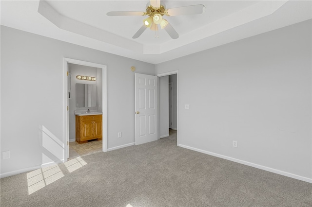 unfurnished bedroom featuring light carpet, ensuite bath, a tray ceiling, ceiling fan, and sink