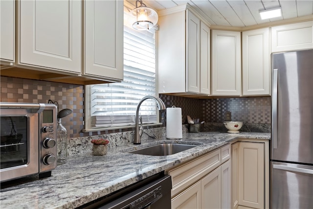 kitchen featuring white cabinets, decorative backsplash, freestanding refrigerator, light stone countertops, and a sink